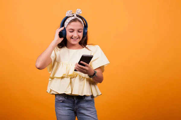 Девочка в жёлтой футболке слушает музыку с телефона и гарнитуры — стоковое фото