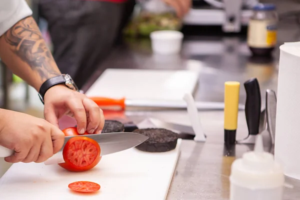 Koch schneidet Tomaten für Burger in Küche — Stockfoto