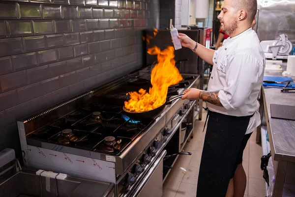 Cozinheiro masculino fazendo marisco inflamatório no fogão na cozinha do restaurante — Fotografia de Stock