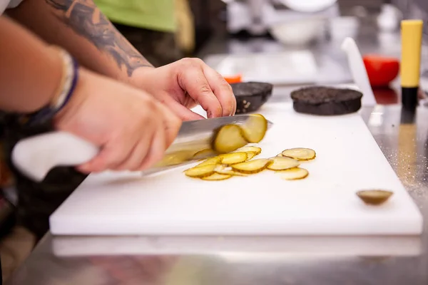 Chef schneidet Essiggurken für leckeren Burger im Restaurant — Stockfoto