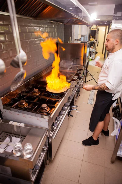 Preparação de alimentos. Chef cozinheiro na cozinha com panela sobre fogão fazendo flambe . — Fotografia de Stock