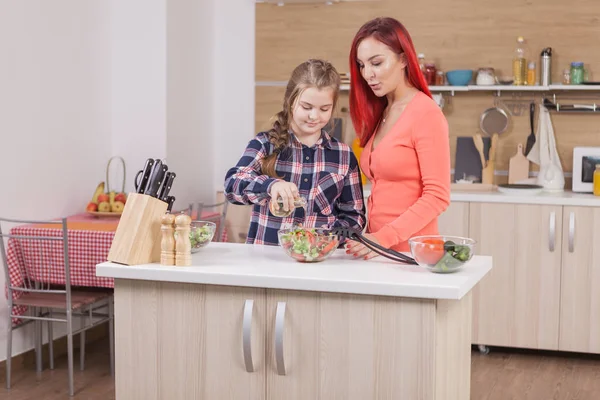 Little girl adding oil to her tasty green salad.