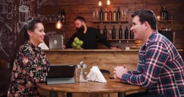 Güzel çift vintage Rustik pub veya kahve dükkanı ahşap duvarlar ile sohbet. Onlar birlikte iyi vakit geçiriyor. Arka planda sakallı bir barista olduğunu
