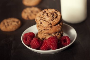 Çikolatalı kurabiye ile kırmızı ahududu ve süt beyaz tabak karanlık eski ahşap tabloda.