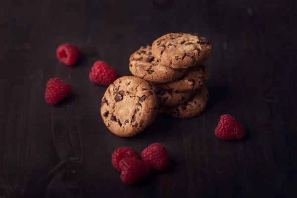 Csokoládé chip cookie-kat a sötét régi fából készült asztal vörös málna. — Stock Fotó