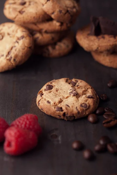 Csokoládé chip cookie-kat, vörös málna és szemes kávé a sötét régi fából készült asztal. — Stock Fotó