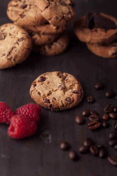 Csokoládé chip cookie-kat, vörös málna és szemes kávé a sötét régi fából készült asztal. — Stock Fotó