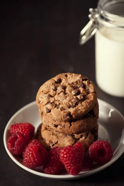 Chocolate chip cookies med röda hallon och mjölk på rustika trä bakgrund. — Stockfoto