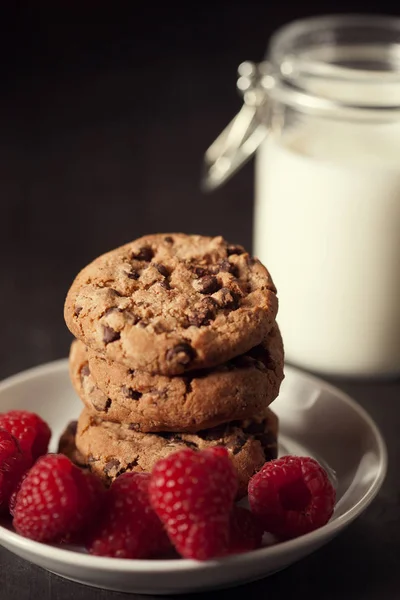 Csokoládé chip cookie-kat, vörös málna és a tej a rusztikus fa háttér. — Stock Fotó