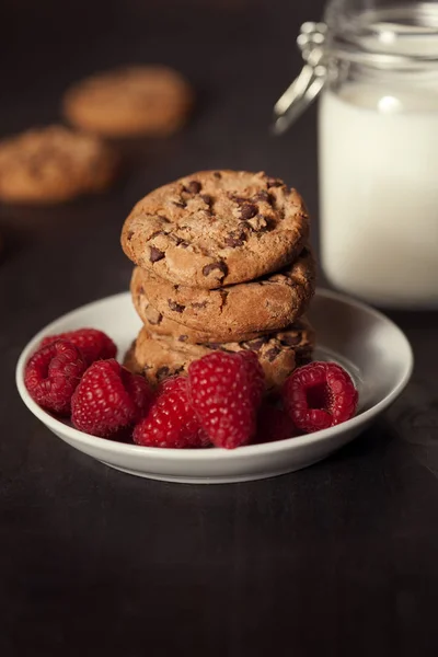 Csokoládé chip cookie-kat, vörös málna és a tej a rusztikus fa háttér. — Stock Fotó