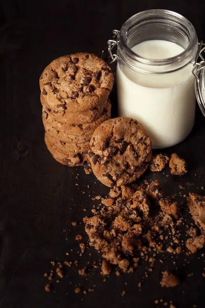 Hemmagjord chocolate chip cookies med flaska mjölk och smulor på rustika träbord. — Stockfoto