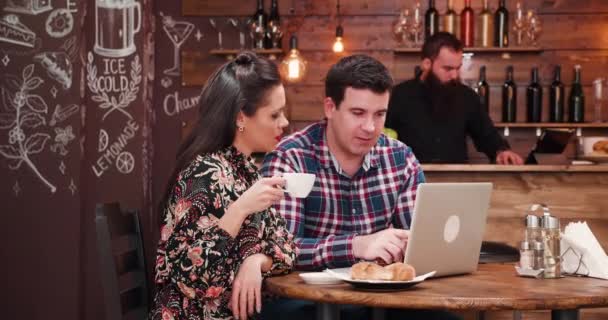 Caucasian couple looking at laptop and drinking coffee with croissants — Stock Video