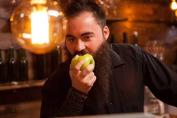 Cantinero barbudo comiendo una manzana verde en un pub vintage —  Fotos de Stock