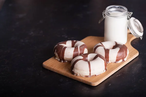 Gestreepte donuts in de buurt van fles melk op donkere houten tafel — Stockfoto