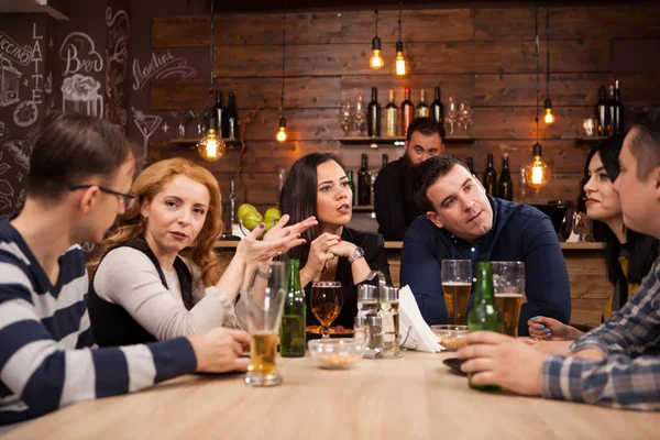 Grupo de jóvenes amigos sentados alrededor de la mesa en el bar juntos —  Fotos de Stock