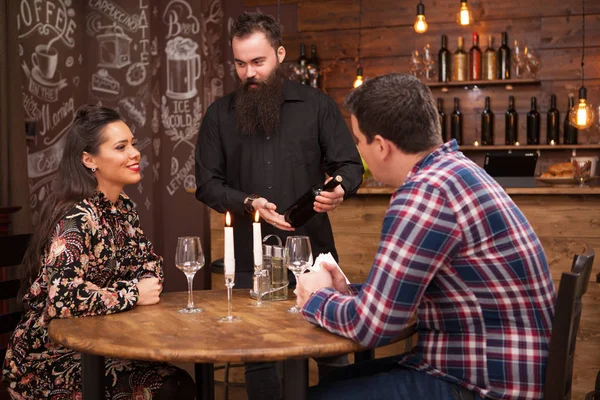 Hipster barbudo barman mostrando uma garrafa de vinho para os clientes — Fotografia de Stock