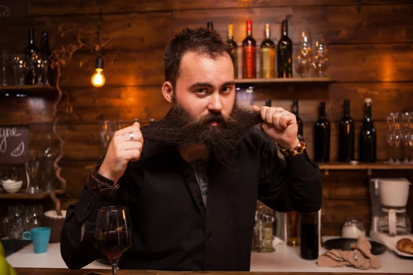 Atractivo camarero jugando con su larga barba detrás del mostrador . —  Fotos de Stock