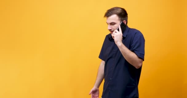 Angry young man in blauw shirt praten aan de telefoon — Stockvideo