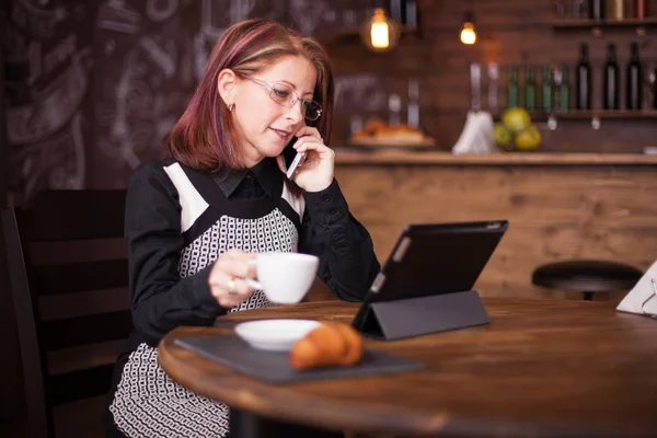 Bir fincan kahve tutarak onu telefonda konuşurken başarılı yetişkin iş kadını — Stok fotoğraf