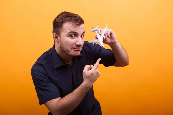 Junger Mann zeigt Spielzeugflugzeug vor gelbem Hintergrund — Stockfoto