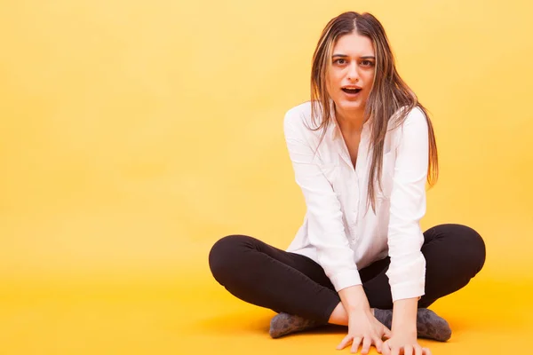 Chockad förvånad ung kvinna i vit skjorta sittande över gul bakgrund — Stockfoto