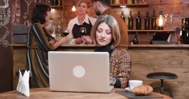 Kobieta, wpisując na swojego laptopa, podczas gdy ludzie są rozmowy w barze — Wideo stockowe