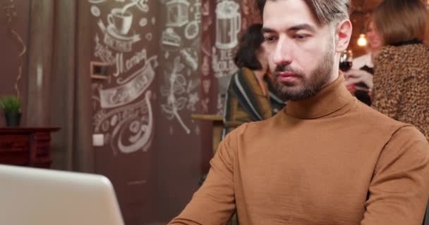 Schöner junger Mann nippt an einem Kaffee, während er an seinem Computer arbeitet — Stockvideo