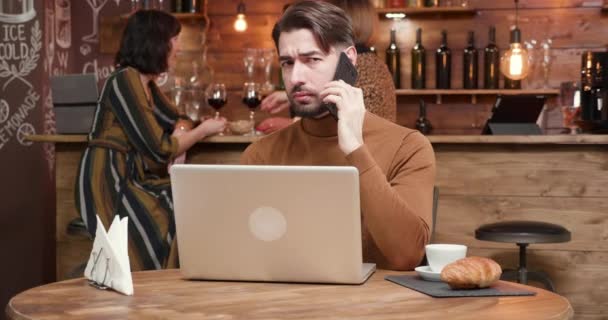 Egy jóképű fiatal üzletember beszél a telefonon a bárban munka közben — Stock videók