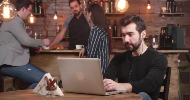 Junger gutaussehender Mann tippt eine Nachricht auf seinen Laptop, während er es sich in einem Vintage-Café gemütlich macht — Stockvideo