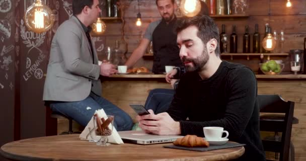 Un giovane uomo messaggia al suo smartphone, afferra il suo computer portatile e lascia il negozio di caffè — Video Stock