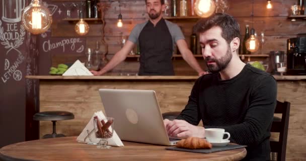 Joven freelancer trabaja y reacciona como nuevos clientes vienen en la cafetería — Vídeo de stock