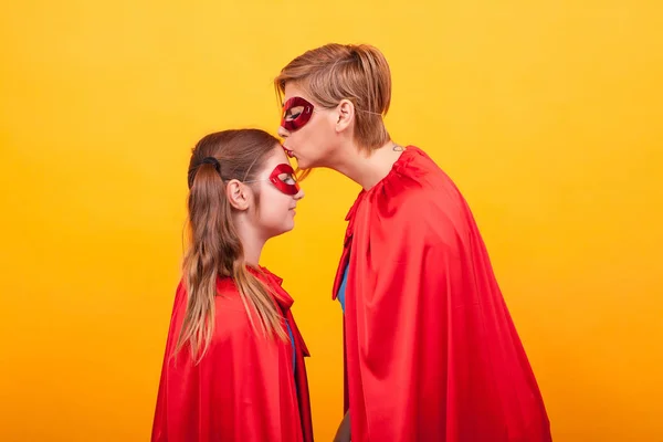 Mother in superman costume kissing his little girl forehead over yellow background