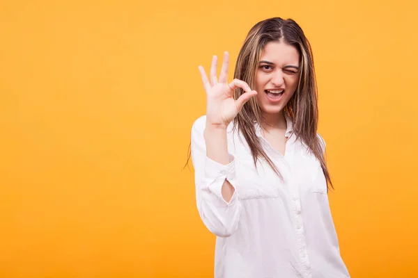 Porträtt av charmiga flicka visar ok tecken och winking över gul bakgrund — Stockfoto