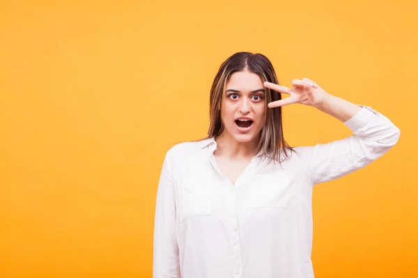 Portrait of girl showing peace sign with her hand on yellow background