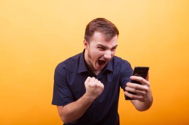 Genç adam sarı arka plan Smartphone'da çığlık