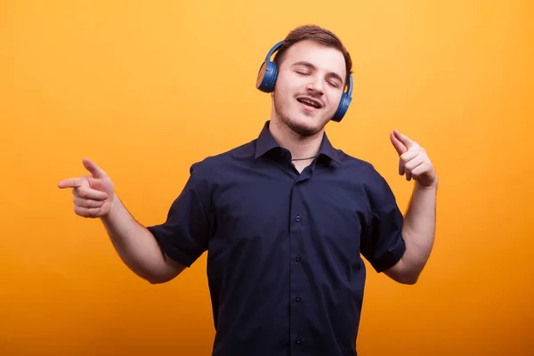 Jovem feliz em camisa azul ouvindo música em fones de ouvido sobre fundo amarelo — Fotografia de Stock