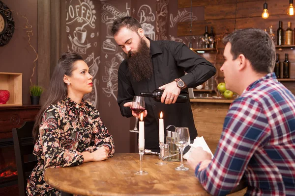 Офіціант наливає червоне вино на красиву пару . — стокове фото