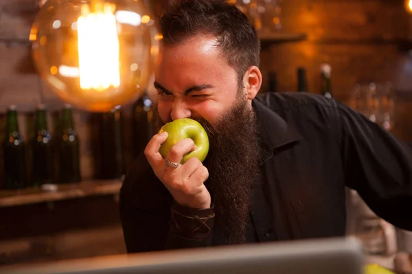 Беардер бармен їсть зелене яблуко в старовинному пабі — стокове фото