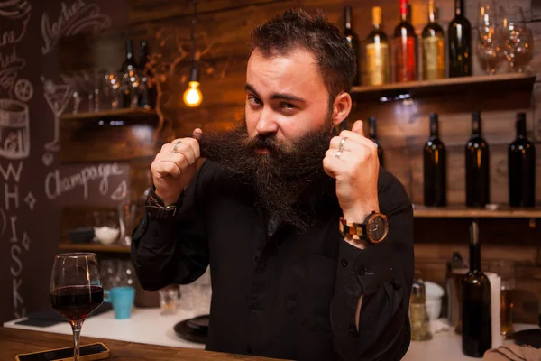 Atractivo camarero jugando con su larga barba detrás del mostrador . —  Fotos de Stock