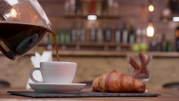 Colpo da vicino di una caffettiera che riempie una tazza da servire con croissant — Video Stock