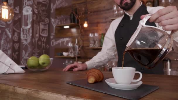 Cuidando suavemente una taza de café recién hecho en una bandeja con un croissant — Vídeo de stock