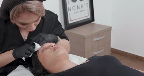 Cosmetologist fêmea nova que limpa as sobrancelhas após o procedimento microblading — Vídeo de Stock