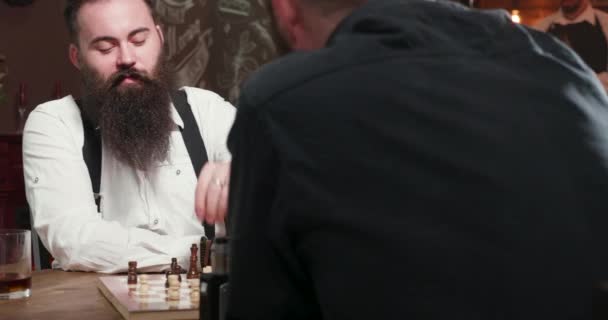 Joven hombre barbudo guapo jugando ajedrez con su amigo en un pub — Vídeos de Stock
