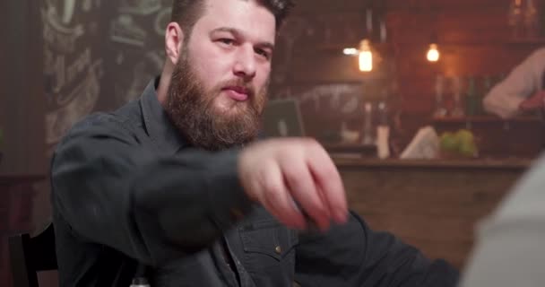 Skäggiga mannen på en bar med en vän dricker från ett glas whisky — Stockvideo