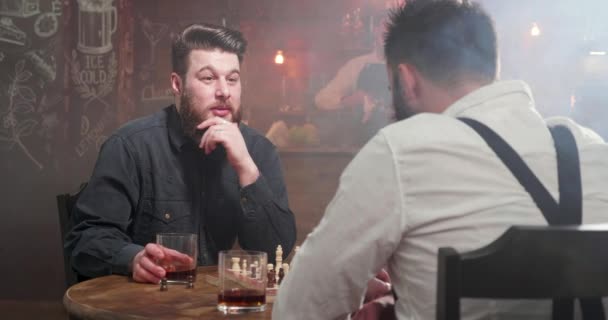 Deux jeunes hipsters prenant des verres de whisky et buvant dans un jeu d'échecs dans un pub — Video