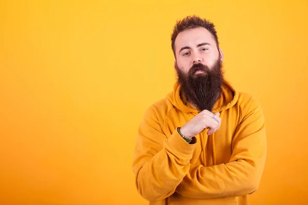 Elegante hipster perline guardando serios la fotocamera e giocando con la barba su sfondo giallo — Foto Stock