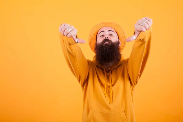 Portrait de hipster barbu avec chapeau montrant pouce vers le bas signe sur fond jaune — Photo