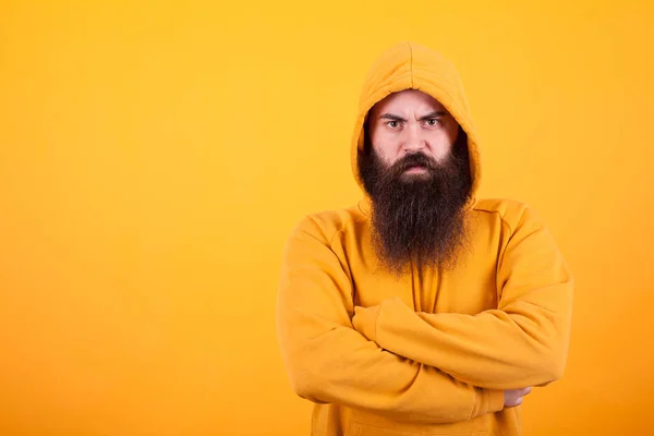 Portrait of dangerous man with long beard wearing a hoodie over yellow background — Stock Photo, Image
