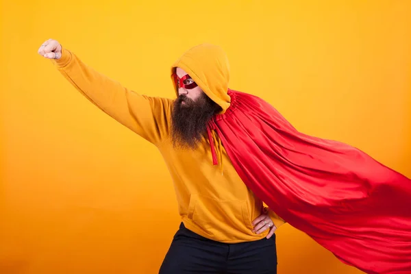 Superhéros avec cape rouge et masque s'envolant en studio sur fond jaune — Photo