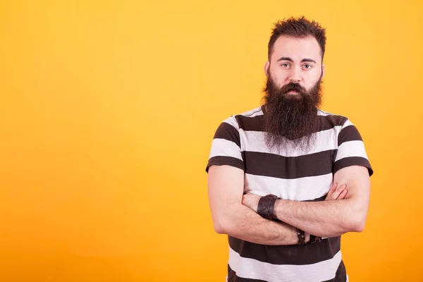 Bel homme barbu avec t-shirt nu tenant les bras croisés et regardant la caméra sur fond jaune — Photo